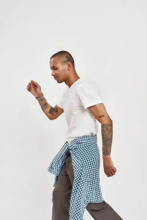 Side view of stylish young mixed race tattooed guy in hip hop casual outfit posing isolated over white backgroundの写真素材