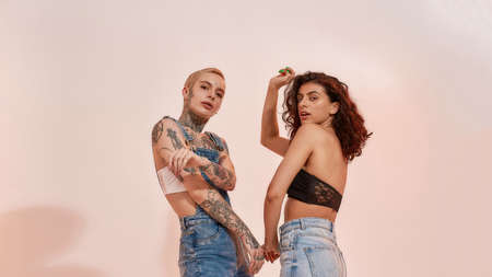 Modern lesbian couple in casual wear dancing together in studio isolated over pink backgroundの写真素材