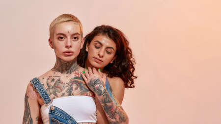 Young diverse women, generation Z lesbian couple embracing while posing together isolated over light pink backgroundの写真素材