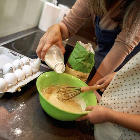 Woman pour milk in bowl during cooking with girlの写真素材