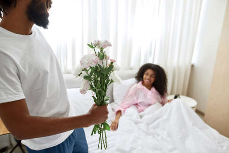 Man with bouquet of flowers near girlfriend in bedの写真素材