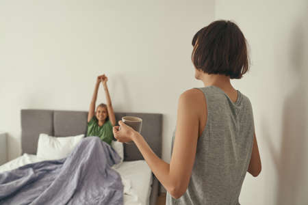 Girl carrying tea to waking up girlfriend in bed