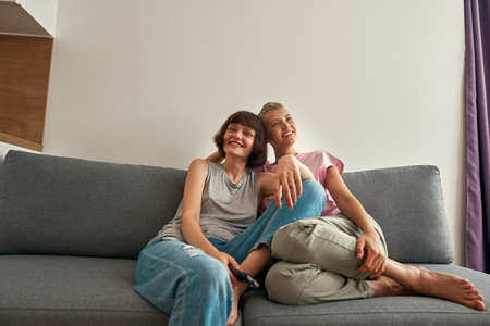 Young smiling lesbian girls watching TV on sofa