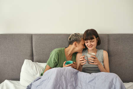Young lesbian couple rest and drink tea on bedの写真素材