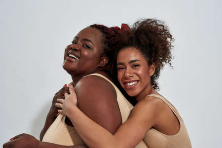 Portrait of two african american women in underwear with different body size having fun while posing together isolated over gray backgroundの写真素材