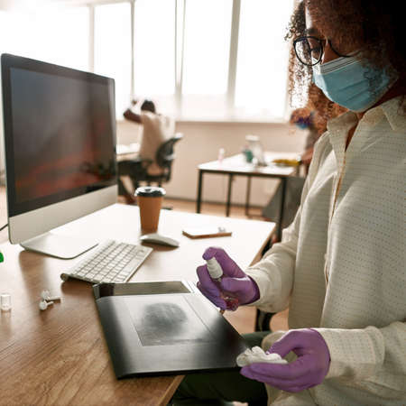 Black woman with sanitizer wiping graphics tablet