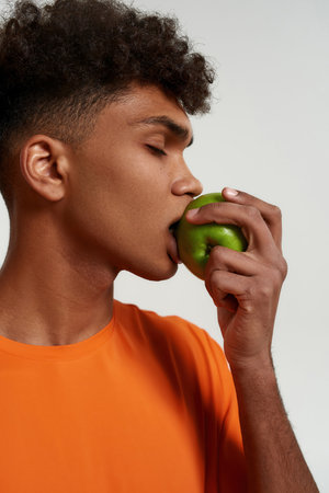 Black man with closed eyes eating delicious apple