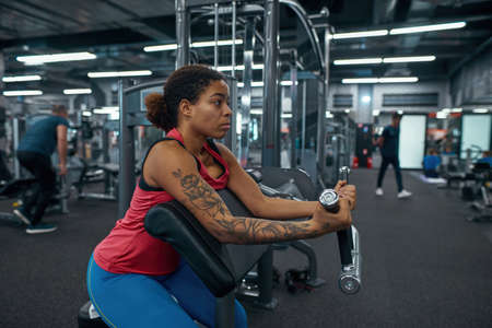 Black girl doing lifting weight for biceps in gym