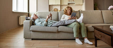 Elderly caucasian couple using gadgets on sofaの写真素材