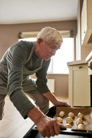 Senior caucasian man putting croissants to ovenの写真素材