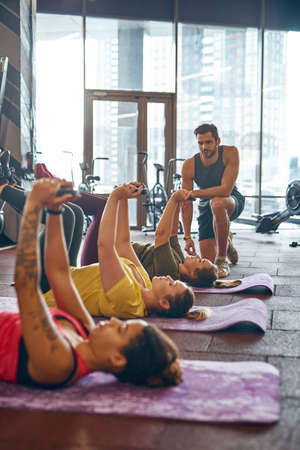 Trainer look at girls do exercise on fitness mats
