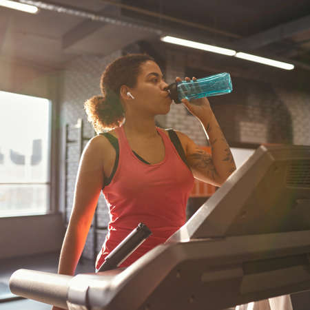 African girl drink water and run on treadmill