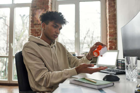 Mixed race male stocks trader taking pills dietary supplement from containerの写真素材