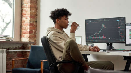African american trader drinks water for body hydration while workingの写真素材