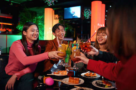 Cheerful asian friends clinking glasses above table at nightclubの写真素材