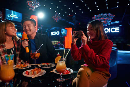 Girl taking photo her friends at karaoke party in club