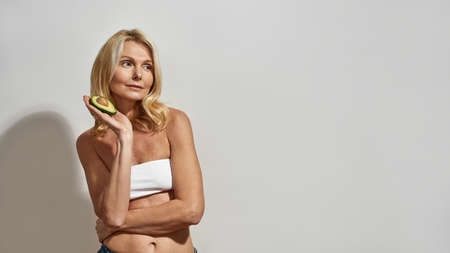 Mature woman holding sliced organic avocado fruitの写真素材