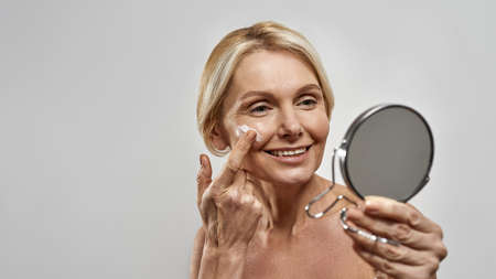 Woman look at mirror and smear cream on her faceの写真素材