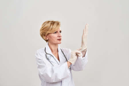 Mature female doctor putting latex glove on handの写真素材