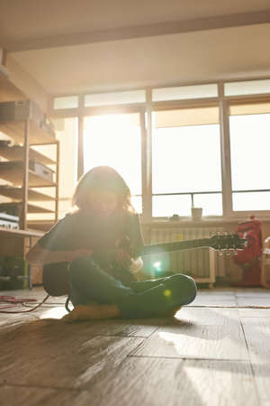Man playing electric guitar on floor at sunny homeの写真素材