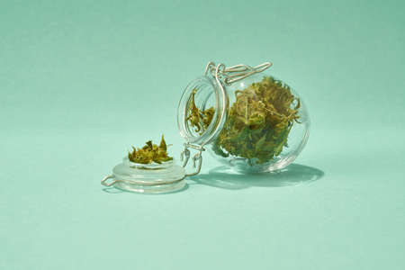 Glass jar with dry marijuana on green backgroundの写真素材