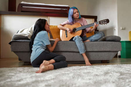 Young happy women playing acoustic guitar for her girlfriendの写真素材