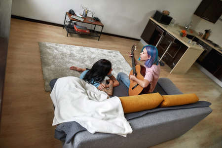 Good moments at home with guitar. Lesbian couple in living roomの写真素材