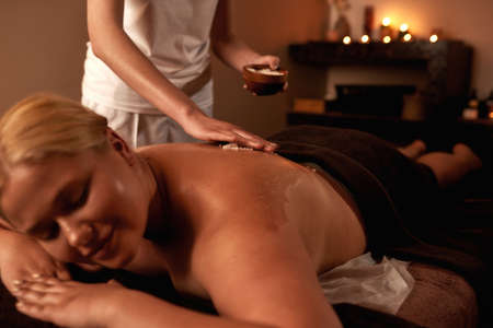 Masseur smearing salt on woman back during scrubの写真素材