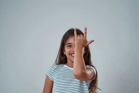 Little girl covering eye with rock sign on face
