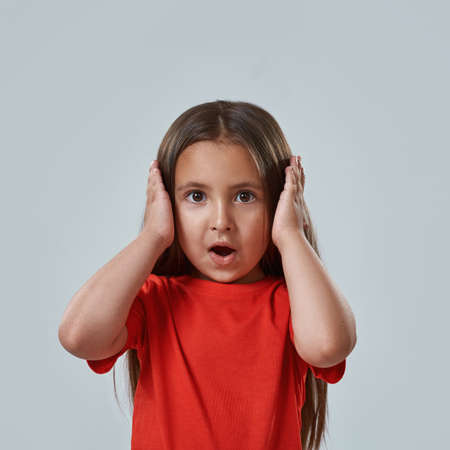 Frightened little girl with open mouth hold headの写真素材