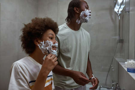Father and son looking at mirror while shavingの写真素材