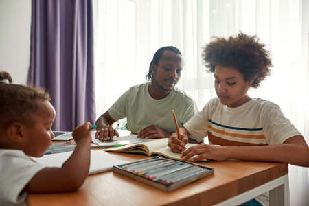 Father and son do homework while little girl drawの写真素材