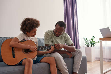 Father teach and help son play on acoustic guitar