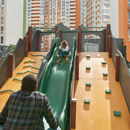 Father catching smiling daughter go down on slide