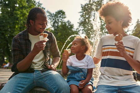Happy family resting with ice cream near fountainの写真素材