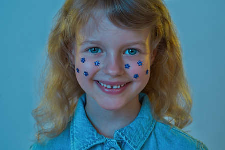 Portrait of smiling little girl with blue flower rhinestones on face looking at cameraの写真素材