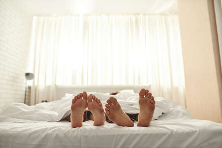 Barefoot feet of couple sleep under blanket on bed