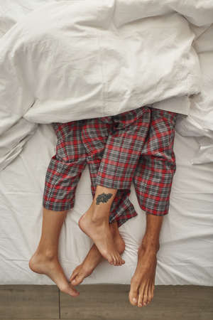 Partial image of couple lying under blanket on bedの写真素材