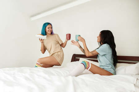 Girl drinking tea or coffee with girlfriend in bedの写真素材