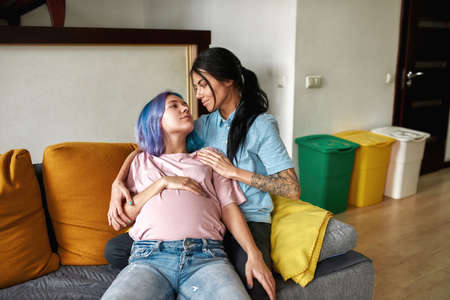 Girl hugging pregnant girlfriend on sofa at home