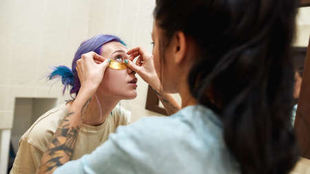 Girl apply under eye patch on face of girlfriend