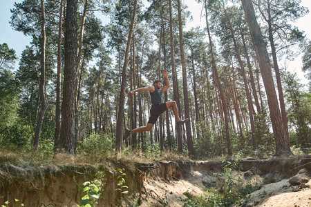 Young sportsman jump over hole while run in forestの写真素材