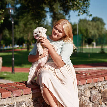 Young joyful girl hold and caress Maltese dog
