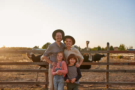 Happy family near paddock with ostriches on ranch