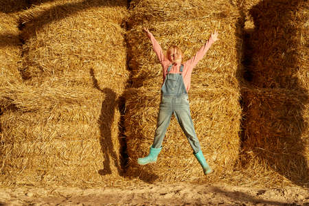 Cheerful girl jumping in barn with fresh hay balesの写真素材