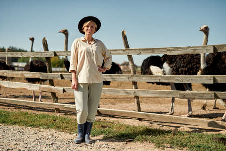 Female farmer near paddock with ostrich on farm