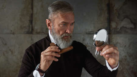 Senior stylish man combing his beard with comb