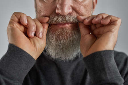 Senior man touching his grey hair beard on faceの写真素材