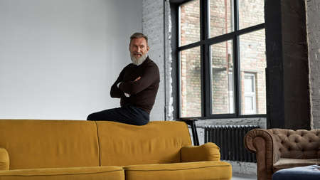 Grey hair man with crossed arms sit on sofa top