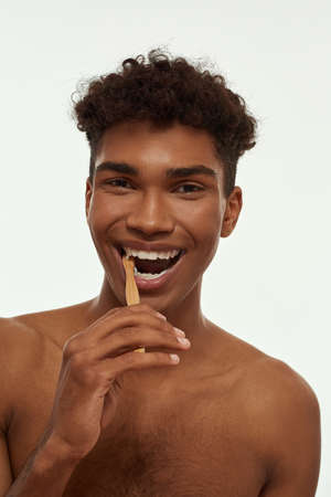 Pleased black guy brushing teeth with toothpaste
